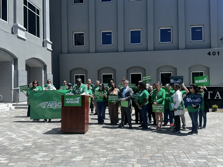 Many AFSCME Local 4041 members in green shirts standing behind a podium in front of the Nevada state legislature and holding rally signs that say Solidairty and State Workers Have Solutions