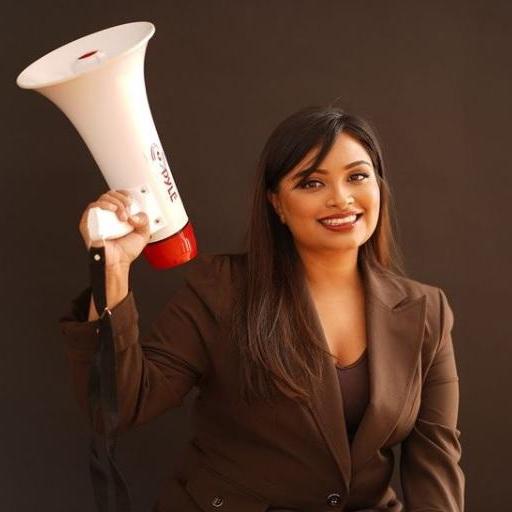 Moumita, a smiling Bangladeshi woman, holds a megaphone in her right hand. She is wearing a brown suit.